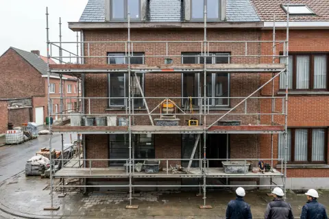 Aluminium stelling met mortelkuipen en emmers tegen een bakstenen gevel van drie bouwlagen